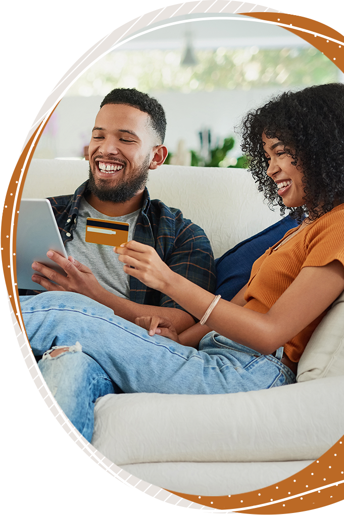 A couple sits on a couch, looking at a tablet and a credit card.